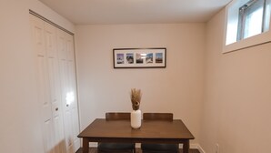 Een eethoek met een houten tafel en bank, een vaas met gedroogde planten en ingelijste foto's aan de muur.