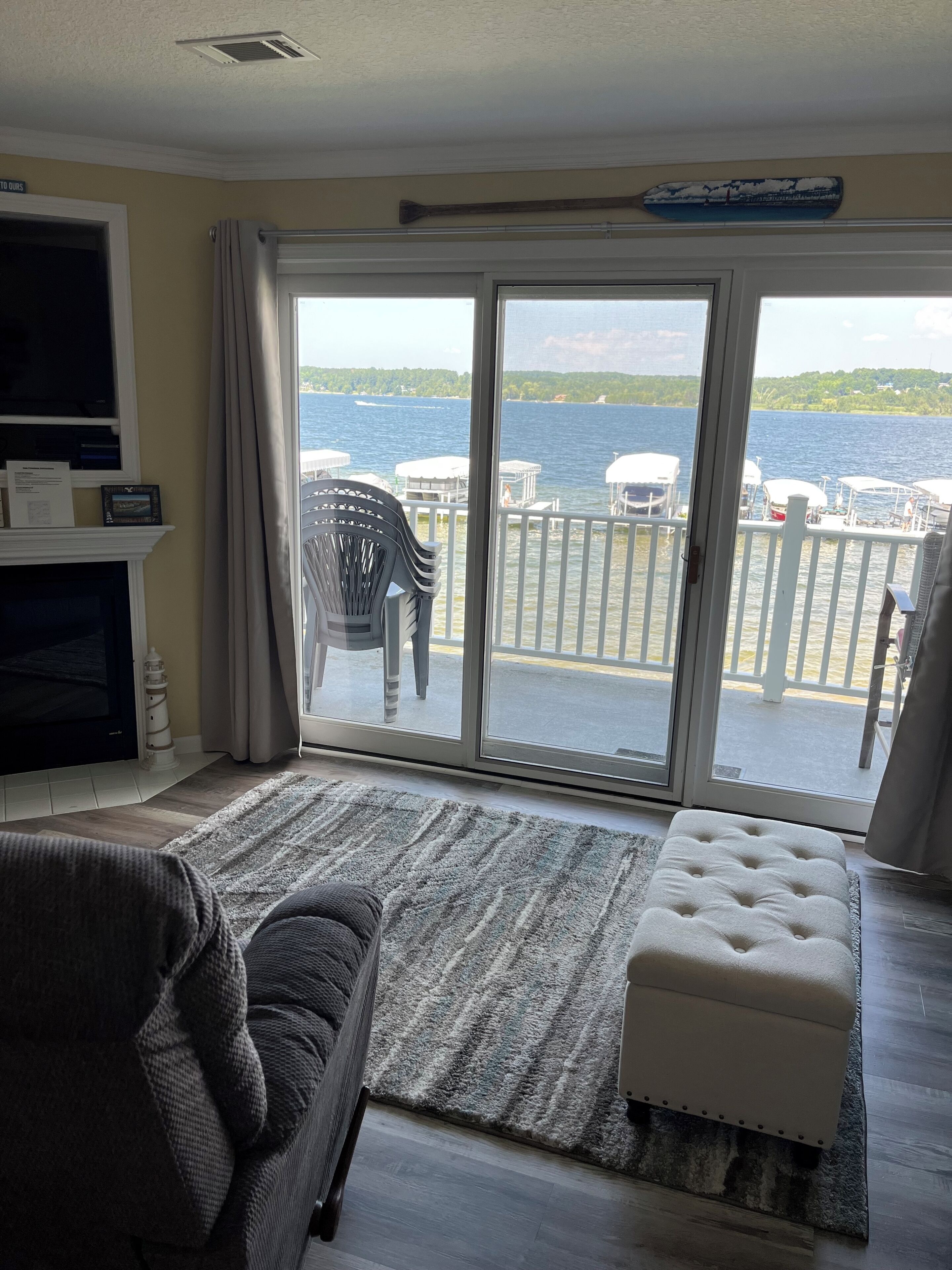 Ein Wohnzimmer mit Sofa, Hocker und Seeblick durch eine Schiebetür.