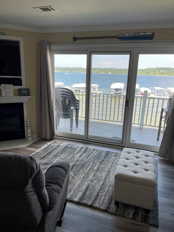 A living room with a sofa, ottoman, and a view of a lake through a sliding glass door.