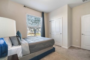 A bedroom with a bed, a window with blinds, a door, and a lamp.