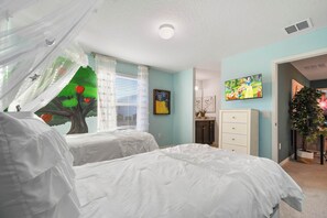 Een slaapkamer met twee bedden, een raam met dunne gordijnen, een plafondlamp, een aan de muur bevestigde televisie en een plant.