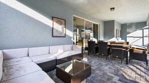 A sunlit patio with a white sofa, wicker chairs, a glass-top table, and a framed botanical print on the wall. - 8BR @ Windsor Island/Star Wars Gameroom/Themed BR (Davenport)
