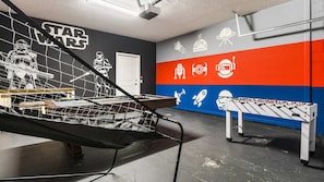 A room with a Star Wars-themed wall, a foosball table, and a pool table.