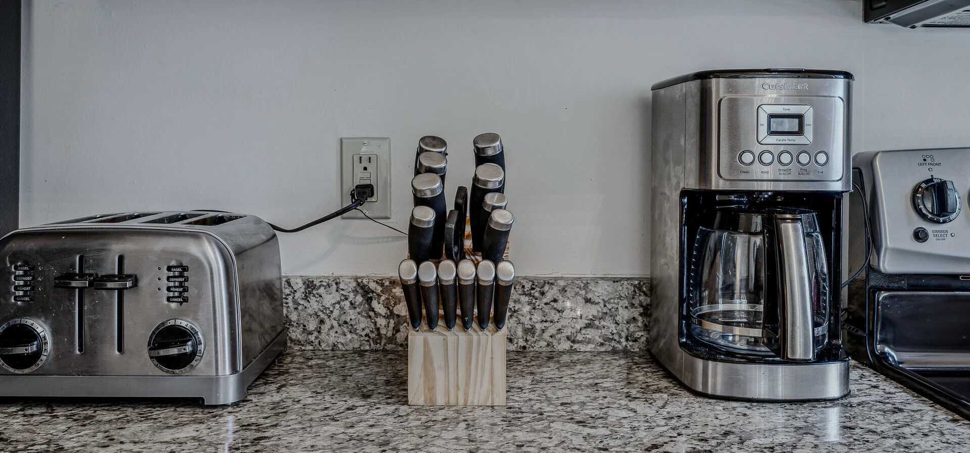 A kitchen with a toaster, a coffee maker, and a knife block on a granite countertop.