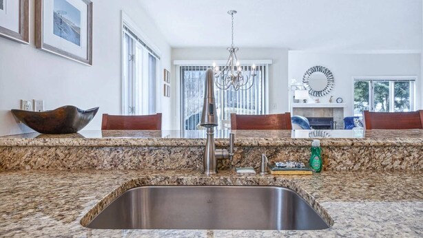 A kitchen with granite countertops, a stainless steel sink, a chandelier, and wooden chairs. - Condo with BBQ, Newton Village (Quechee)