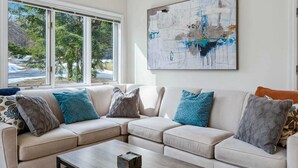 A living room with a beige sectional sofa, a coffee table, and a large abstract painting on the wall. - Condo with BBQ, Newton Village (Quechee)