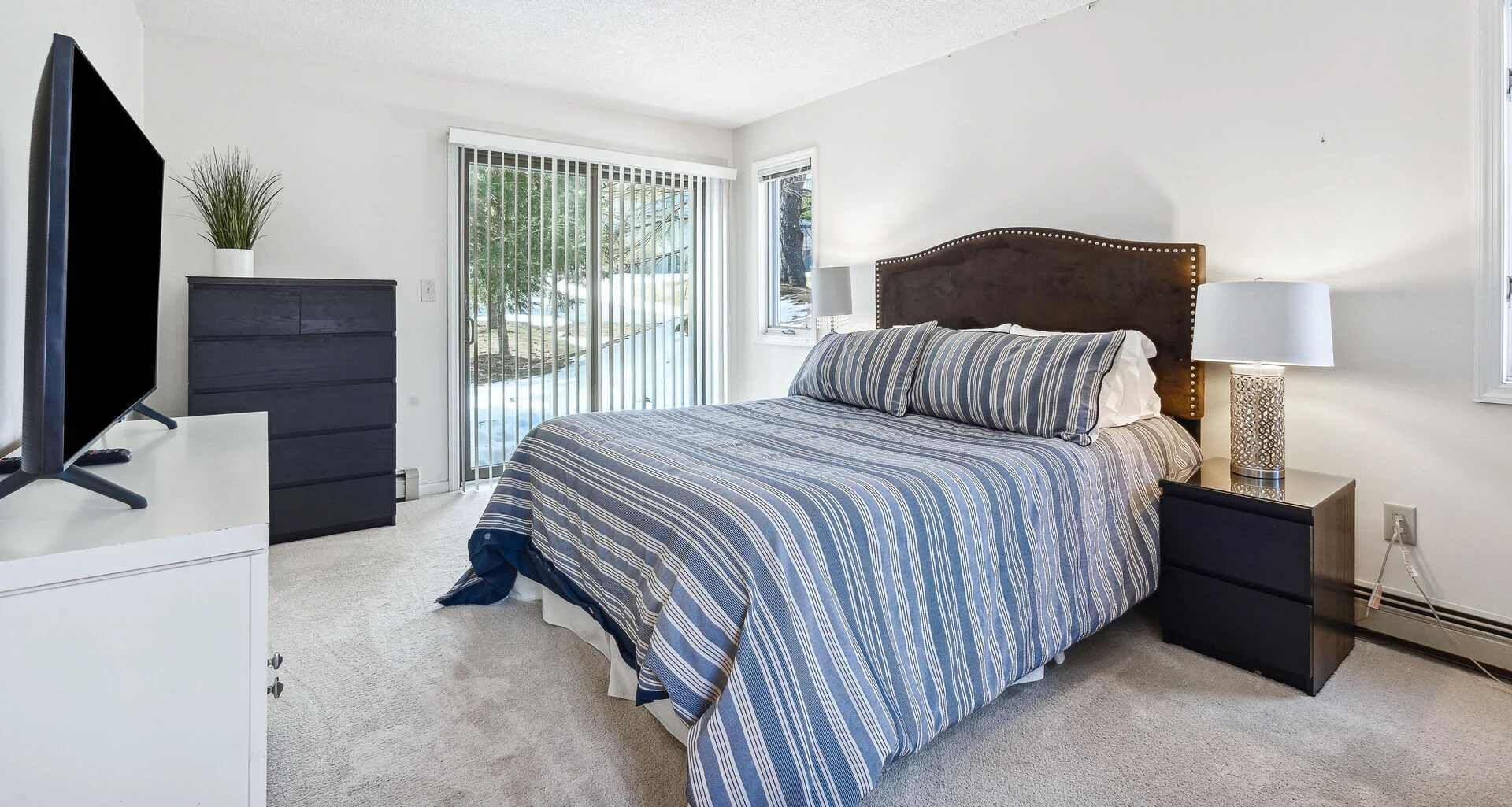 A bedroom with a bed, a TV, a dresser, and a lamp.