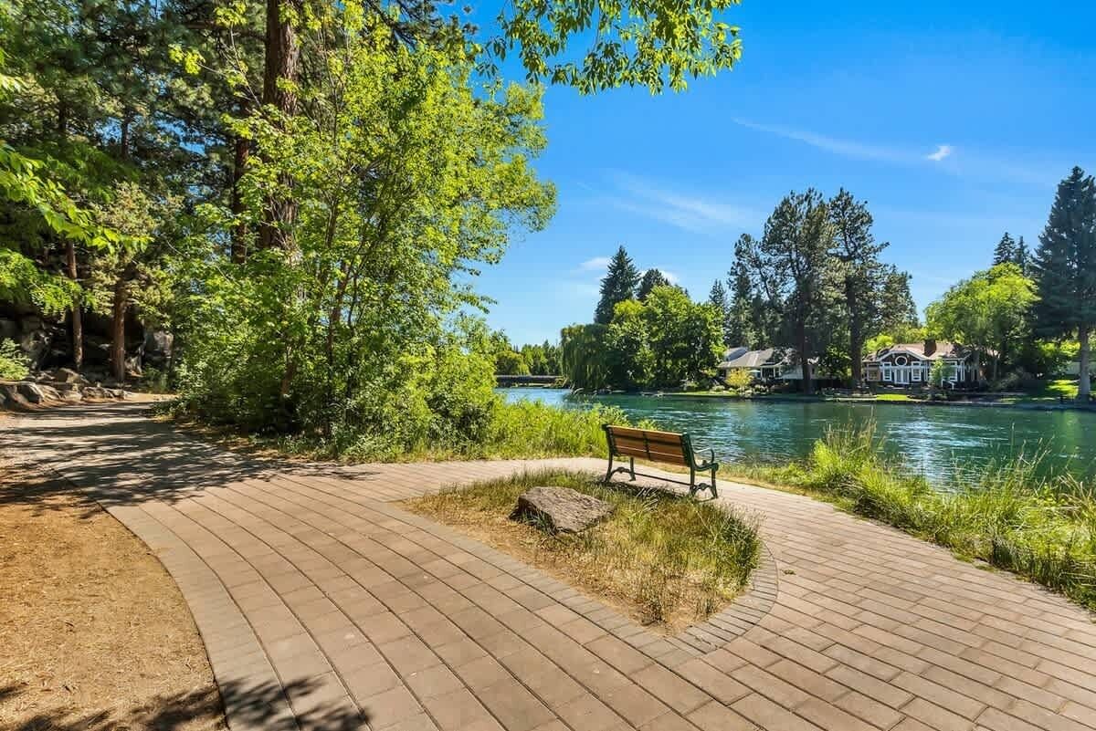 Un parc avec un sentier dallé, un banc et une rivière.
