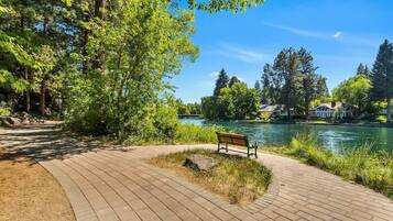 Un parc avec un sentier dallé, un banc et une rivière.