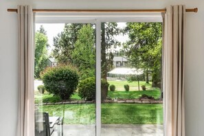 A view through a sliding glass door with a wooden frame, leading to a well-maintained lawn and trees.
