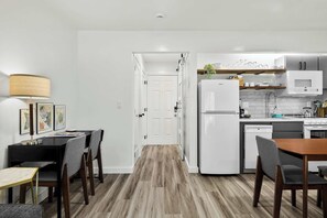 A modern kitchen with white appliances, a dining area with a table and chairs, and a hallway leading to a door.