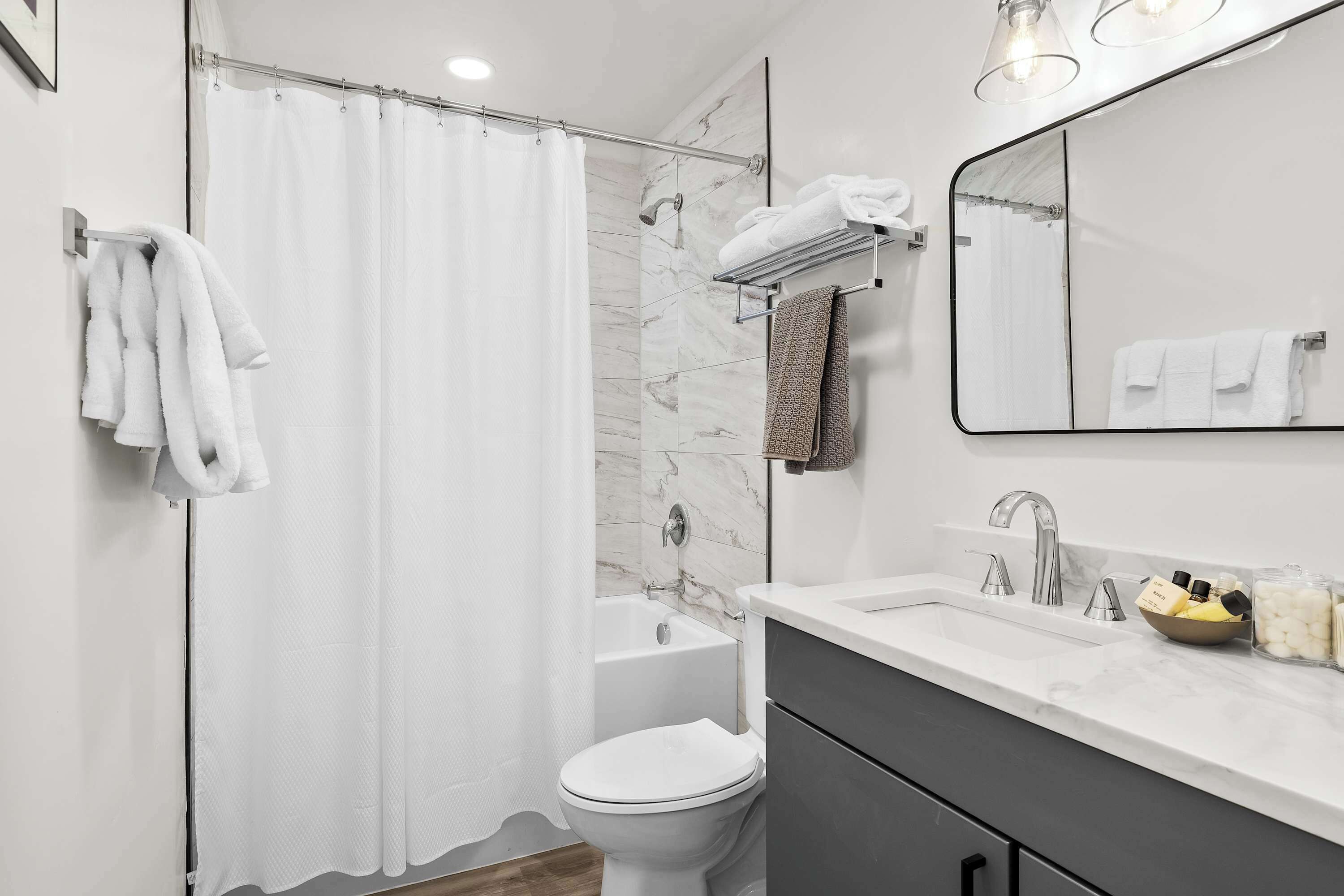 Une salle de bain moderne équipée d’une douche, de toilettes et d’un lavabo, avec des murs en marbre et un grand miroir.