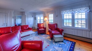 Une pièce comprenant un canapé en cuir rouge, un fauteuil assorti, un petit pouf, une table basse blanche et un tapis à motifs.