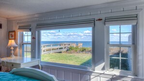 Une chambre avec une grande fenêtre donnant sur une terrasse en bois et l’océan.