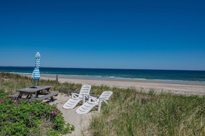 Ein Strand mit einer Holzbank, einem gestreiften Sonnenschirm und weißen Liegestühlen.