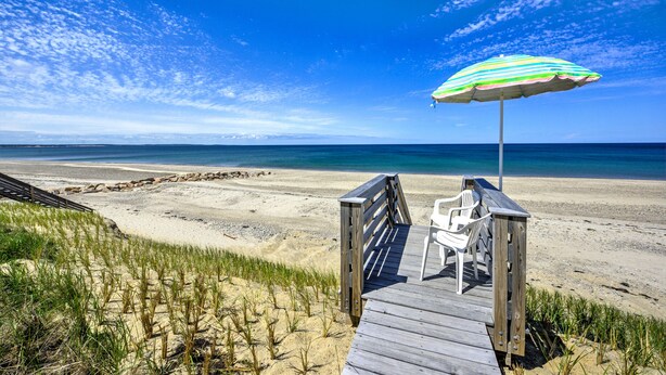 Een houten looppad leidt naar strandstoelen onder een gestreepte parasol.