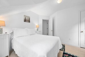 Une chambre à coucher avec un grand lit, deux tables de chevet avec des lampes, une porte et un petit tapis.