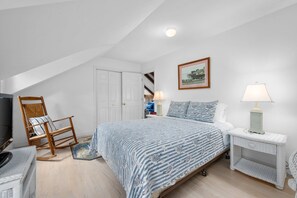 A bedroom with a bed, a rocking chair, a television, and a white door. - Sun & Serenity at A Wave From It All (Pocasset)