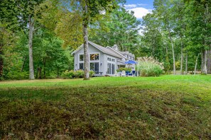 A house with a porch, surrounded by trees and grass. - Sun & Serenity at A Wave From It All (Pocasset)