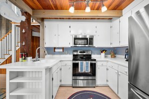 A modern kitchen with white cabinets, a stainless steel refrigerator, a microwave, and an oven. - Sun & Serenity at A Wave From It All (Pocasset)