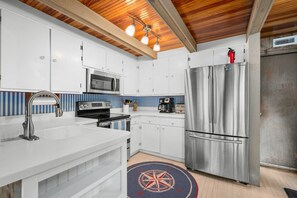 A modern kitchen with white cabinetry, stainless steel appliances, and a wooden ceiling. - Sun & Serenity at A Wave From It All (Pocasset)