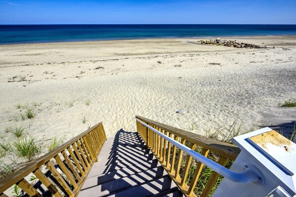 Un escalier en bois mène à une plage d’où l’on a une vue dégagée sur l’océan.