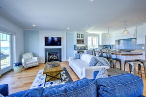 Un salon moderne avec un canapé blanc, une table basse et une cheminée. On y trouve également un coin cuisine avec des meubles blancs et un plan de travail bleu.