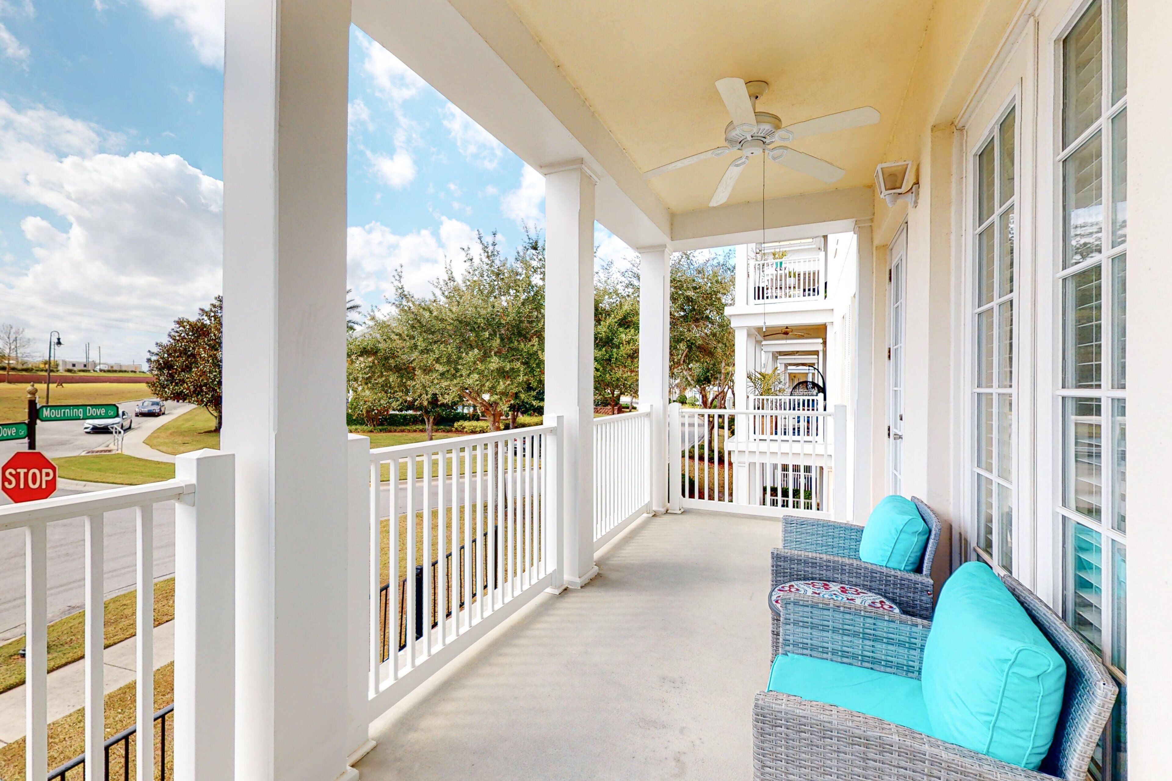 A covered porch with a ceiling fan, white railings, and a wicker sofa with cushions.