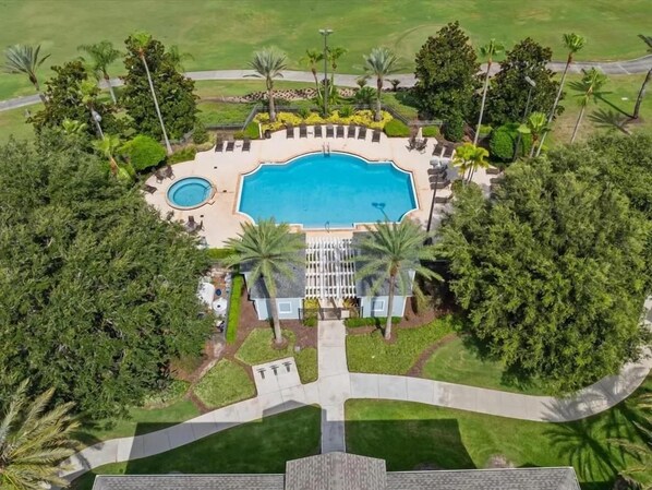 An aerial view of a resort with a central swimming pool, lounge areas, and palm trees.