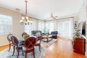 A spacious living room with a dining area, a ceiling fan, and large windows.