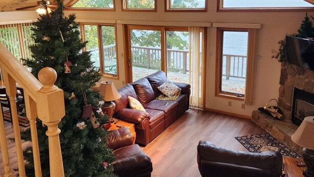 A spacious living room with a large wooden ceiling, a fireplace, a Christmas tree, and a view of the lake through large windows. - Lakefront Deck w/ Unmatched View and Location - New Deck (Garrison)