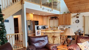 A spacious living area with leather sofas, a wooden staircase, a kitchen with wooden cabinets, and a dining area. - Lakefront Deck w/ Unmatched View and Location - New Deck (Garrison)