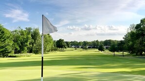 A golf course with a flagstick in the foreground, surrounded by well-maintained grass and trees. - Lakefront Deck w/ Unmatched View and Location - New Deck (Garrison)