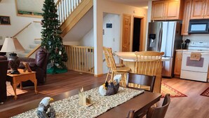 A spacious dining area with a wooden table and chairs, a Christmas tree, and a kitchen in the background. - Lakefront Deck w/ Unmatched View and Location - New Deck (Garrison)