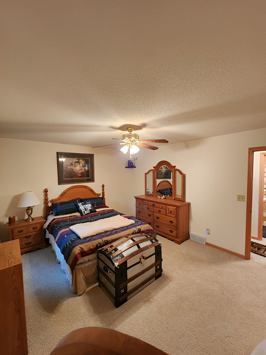 Une chambre à coucher avec un lit, une commode, un miroir, un ventilateur de plafond et un tableau encadré accroché au mur.