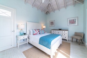 A bedroom with a white bed, two bedside tables with lamps, a dresser, a chair, and artwork on the walls.