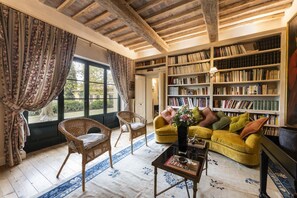 Uma sala de estar acolhedora com uma grande estante, cadeiras de vime, um sofá amarelo e um tapete azul estampado.