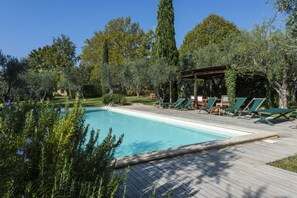A pool with lounge chairs, surrounded by greenery and trees.