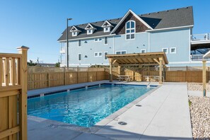 A swimming pool with a wooden deck and a covered seating area, surrounded by a wooden fence.