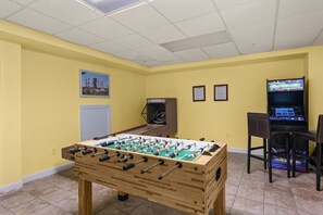 A room with a foosball table, a television, and a small table with chairs.