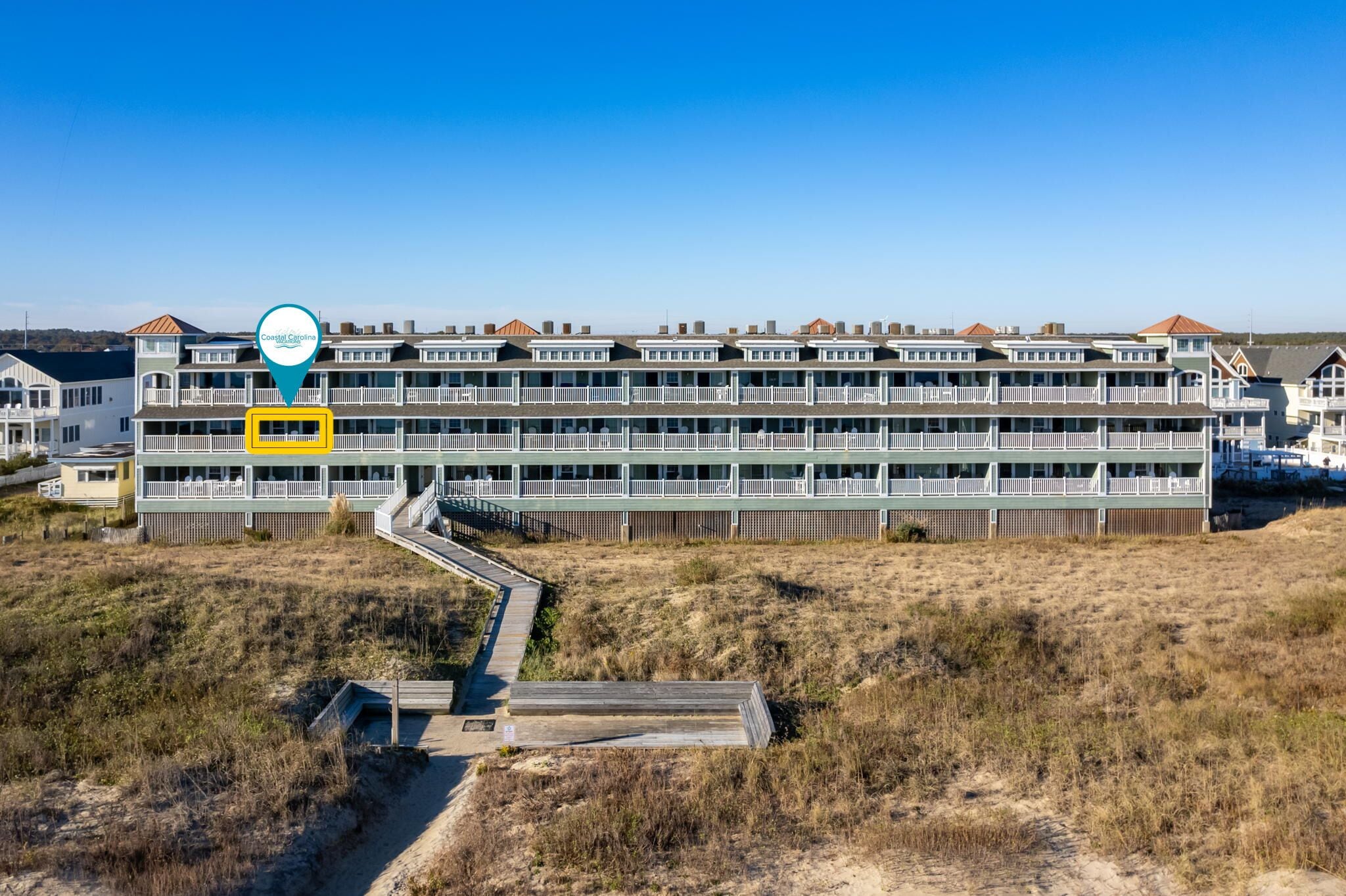 A coastal hotel with multiple floors, a wooden deck, and a clear view of the beach.
