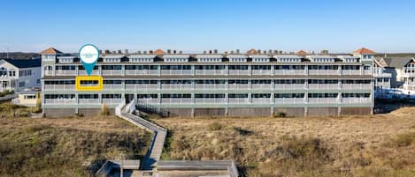 A coastal hotel with multiple floors, a wooden deck, and a clear view of the beach.
