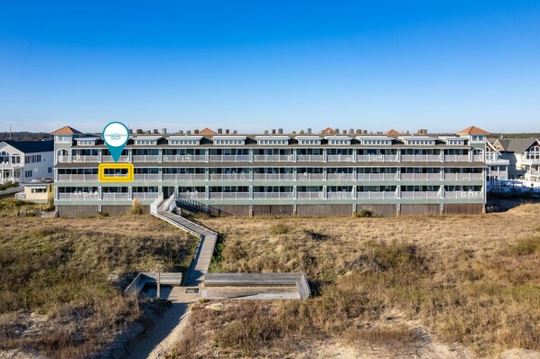 A coastal hotel with multiple floors, a wooden deck, and a clear view of the beach.