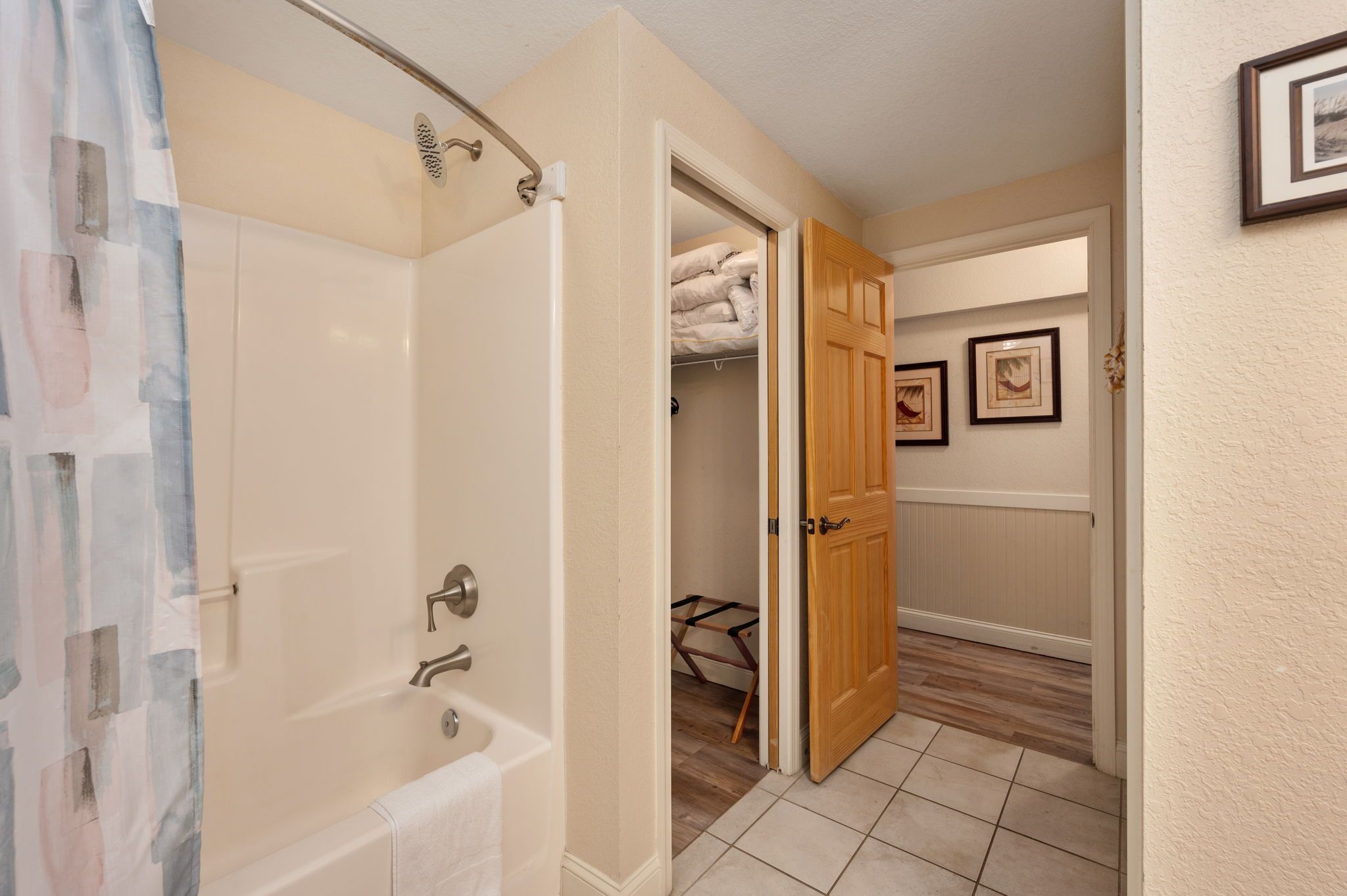 A bathroom with a bathtub, a shower curtain, and a wooden door leading to a closet with a bed.