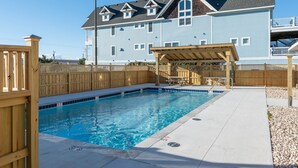 Une piscine dotée d’une terrasse en bois et d’un espace salon couvert, le tout entouré d’une clôture en bois.