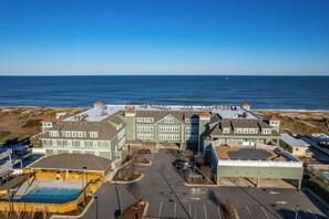 A coastal hotel with multiple buildings, a parking lot, and a pool area. - First Flight Retreat 215: Oceanfront condo, Great Views & Easy Walk to Beach! (Kill Devil Hills)