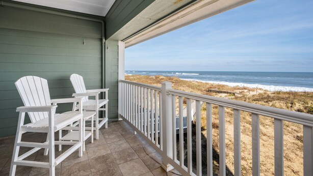 Un balcon avec des fauteuils Adirondack blancs et une vue sur la plage.