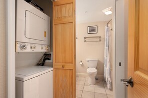 A laundry room with a washing machine and dryer, a wooden door, a toilet, and a shower curtain.