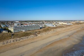 An aerial view of a coastal town with a prominent hotel building featuring multiple floors and a flat roof.