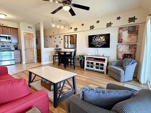 Una sala de estar moderna con comedor, cocina y un televisor mostrando 'Coastal Carolina Vacations and Sales'.